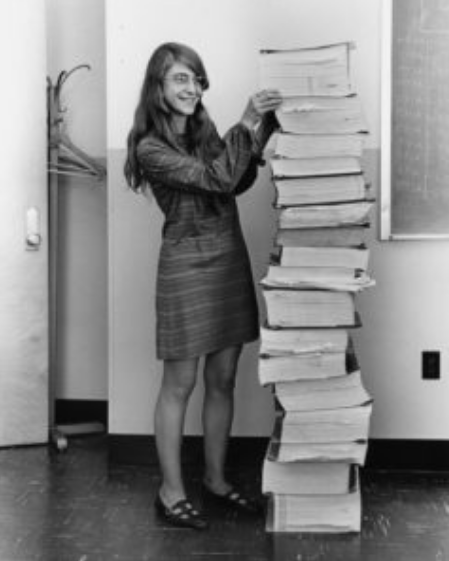 **Figure: Hamilton instigated HITL work at NASA** Margaret Hamilton stands next to a stack of program listings from the Apollo Guidance Computer in a photograph taken in 1969.  --- Image Credit: Wikimedia Commons.