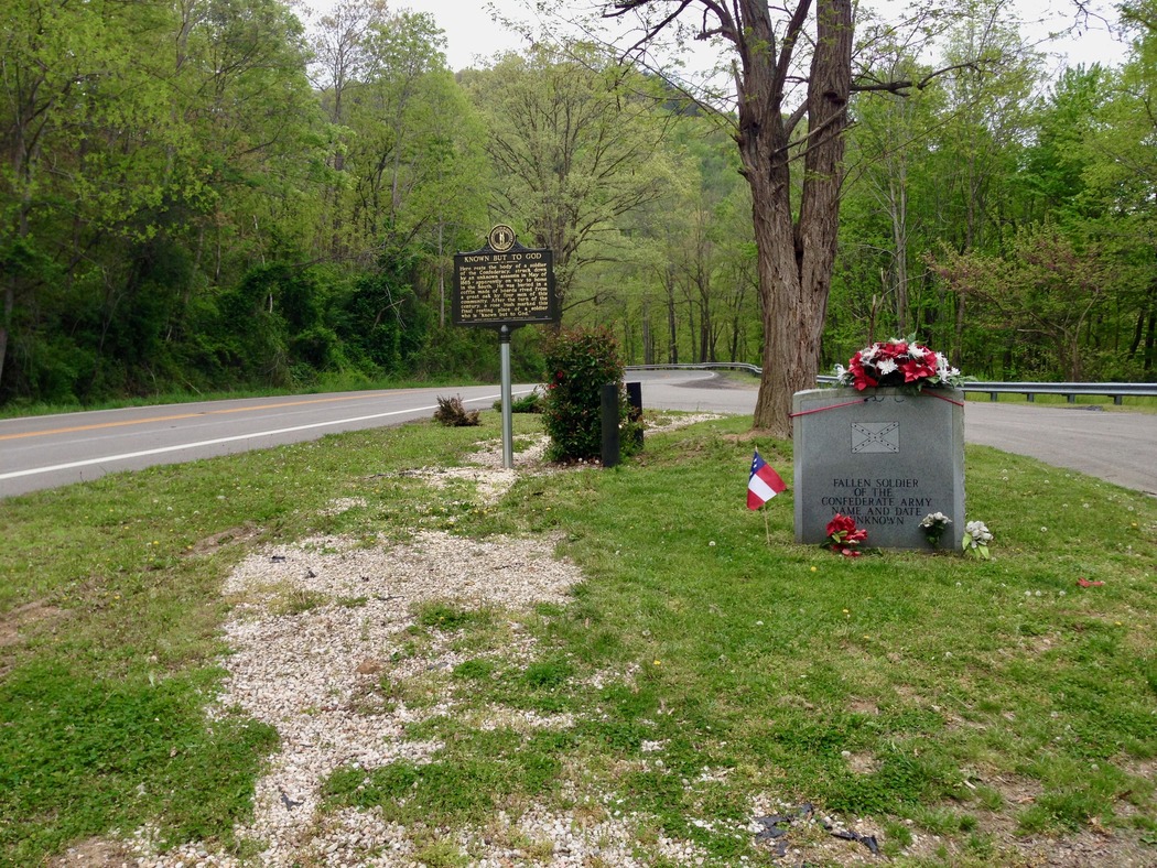 Burial place with modern granite headstone and century-old memorial rosebush and waypoint marker sign